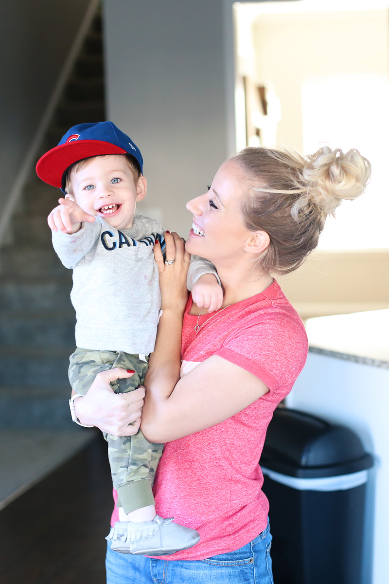 A baby boy, held by his smiling mother, grins and points to the camera.