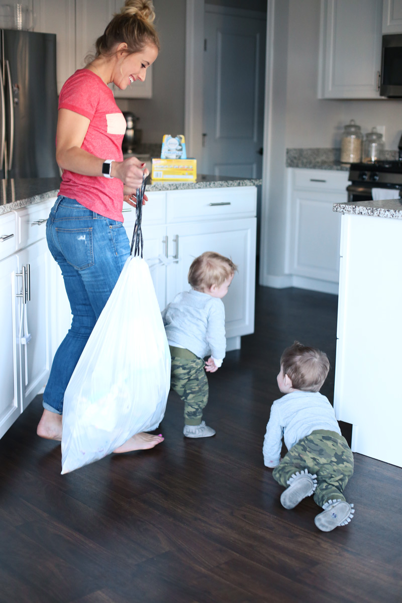 A mother happily holds a trash bag as she smiles at her two toddlers.