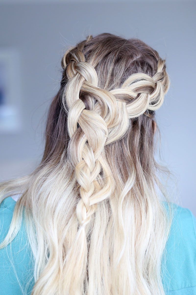 A close-up photo of a blonde woman facing away from the camera, her hair cascading down her back. Two braids come around each side of her head and meet at the back. Dutch braid hairstyles tutorial.