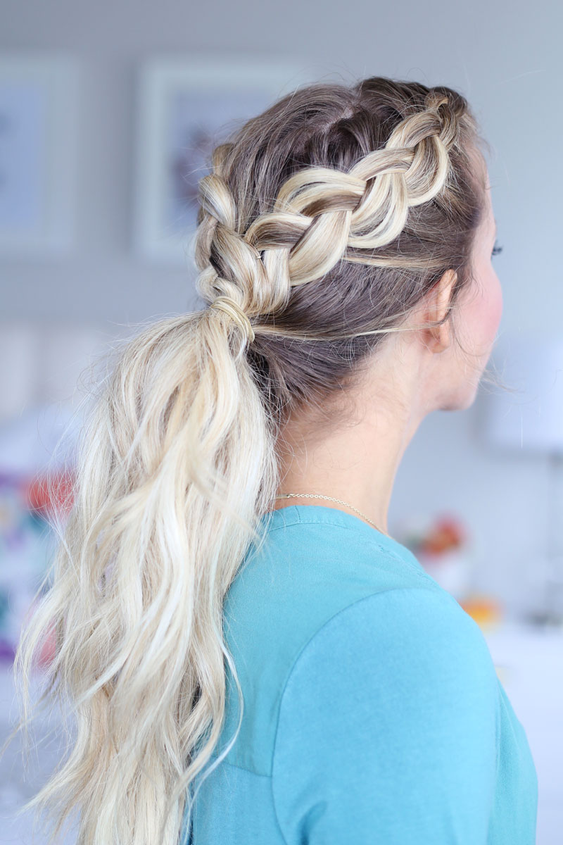 A side-view of a blonde woman with two braids, one on each side of her head. The braids meet in a long ponytail down her back. Dutch braid hairstyles tutorial.