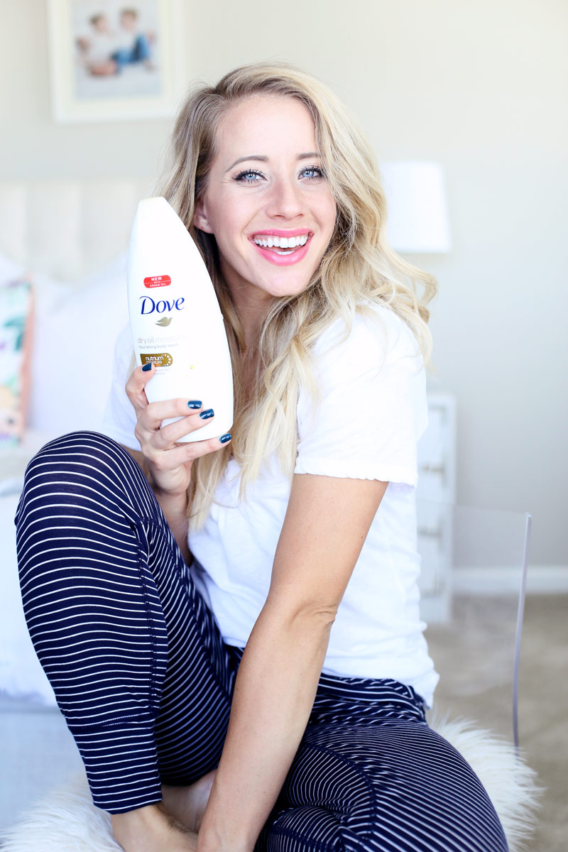 A woman smiles happily and holds a bottle of Dove's Dry Oil Moisture Body Wash.