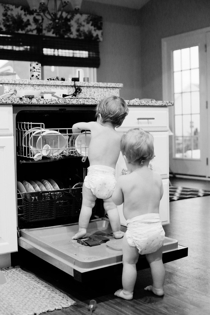 A sepia photo of toddlers in diapers loading a dishwasher.