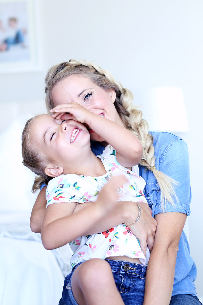 Abby sits with her daughter on their back, both laughing. Love your hair with Twist Me Pretty.