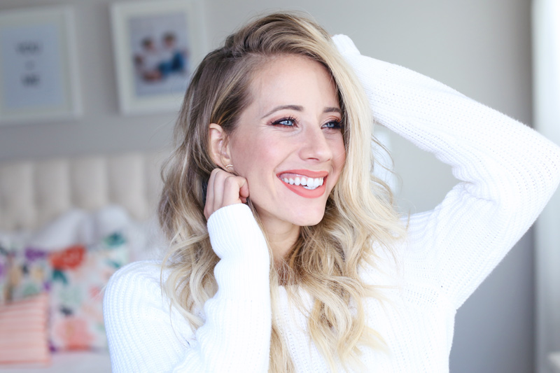 A blonde woman with copper eye-shadow and coral-lip-stick smiles as she looks into the distance. Fall-inspired make-up tutorial.