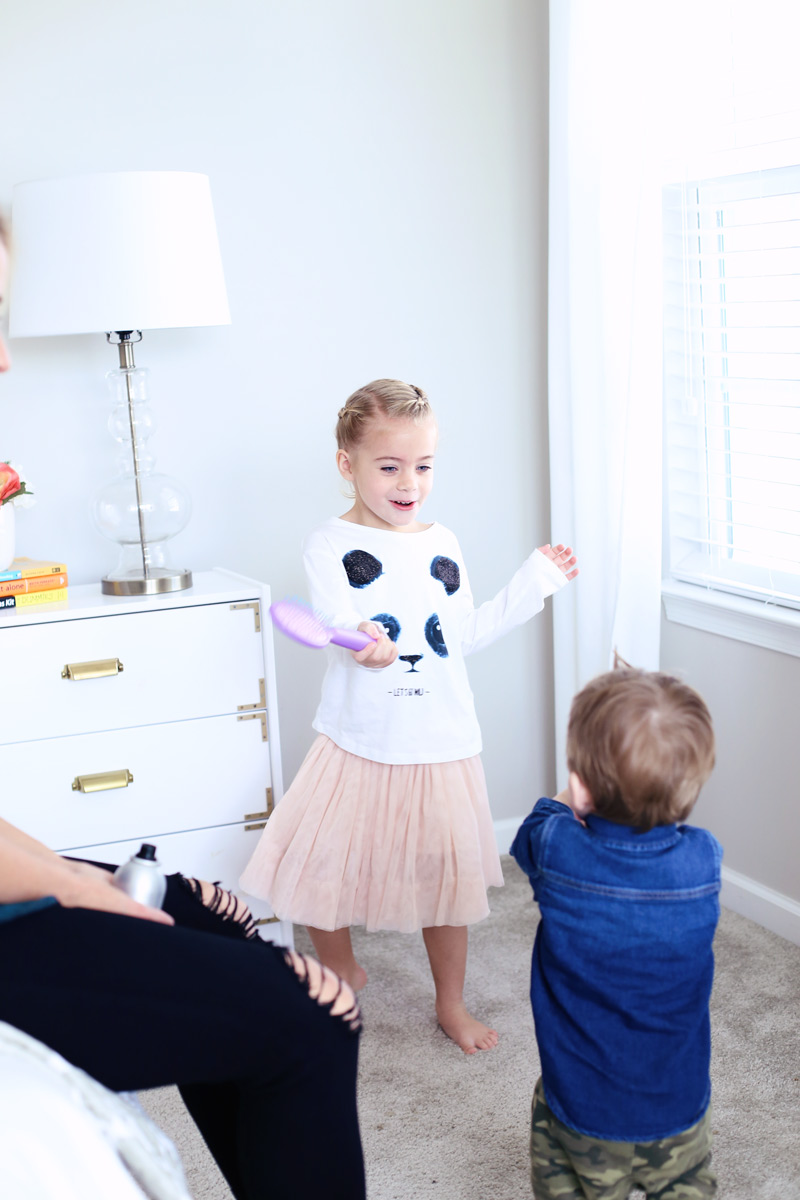 A little girl smiles and dances with a hair brush, looking at her little brother. Twist Me Pretty - Our Morning Routine.