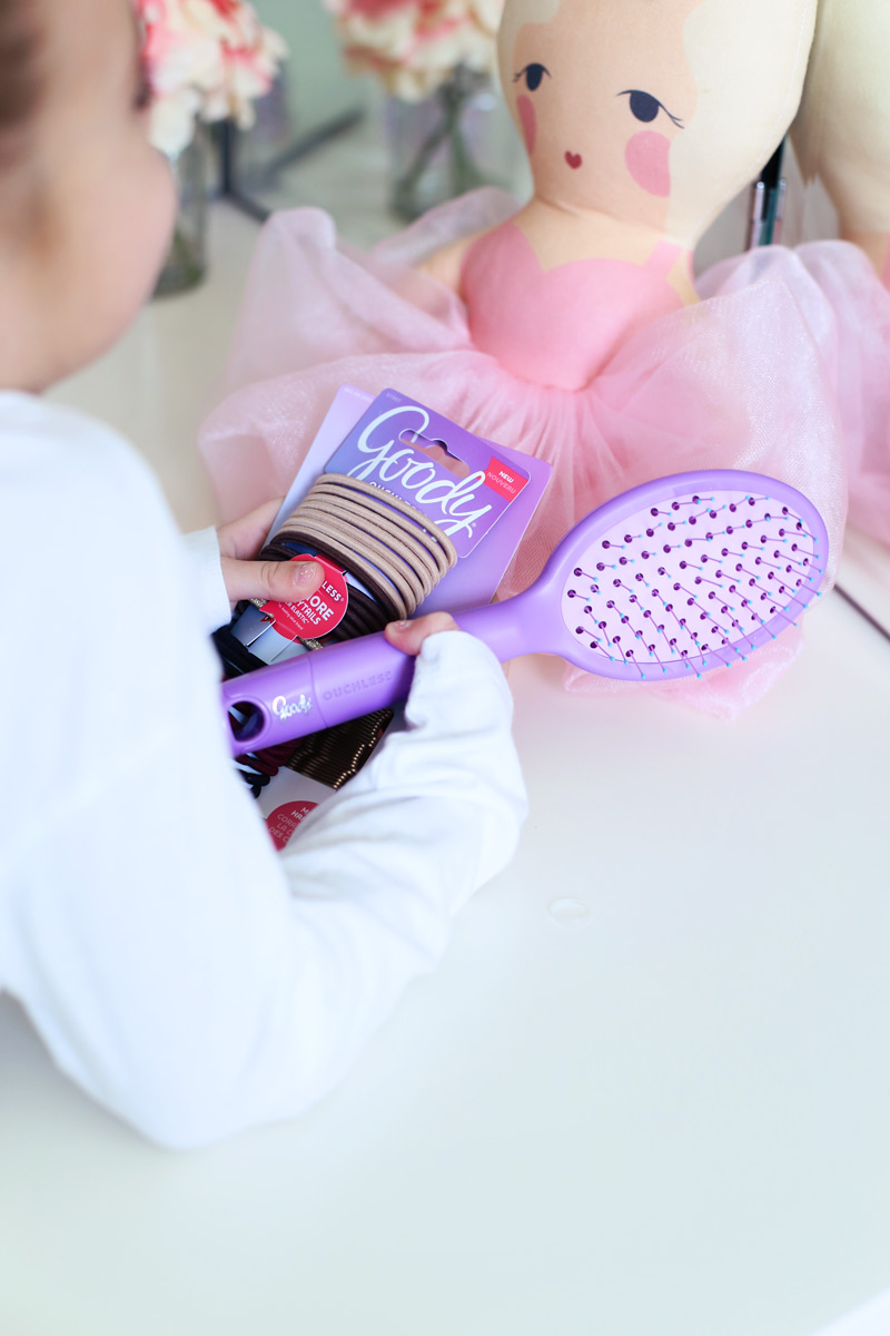 Twist Me Pretty - Our Morning Routine A little girl faces a doll and holds Goody brand hair ties.