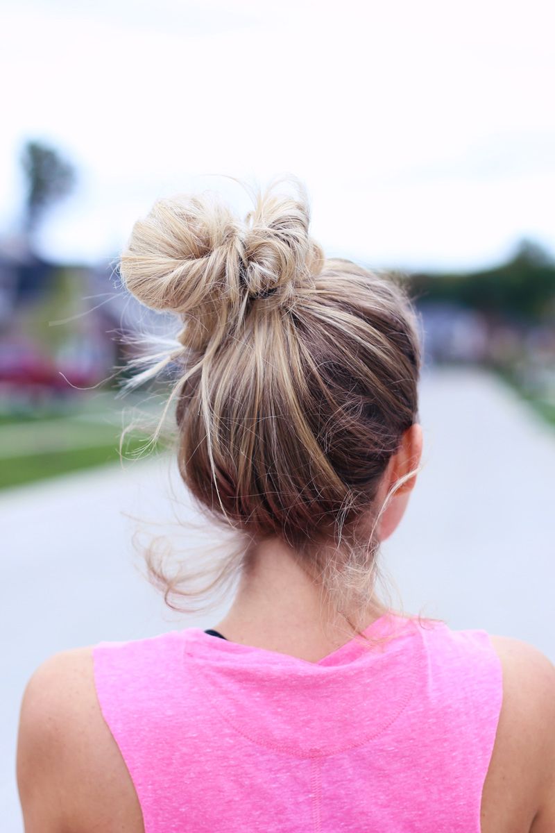 A woman looks away from the camera. We see her blonde top knot. The perfect hair style when you're staying in shape. Twist Me Pretty.