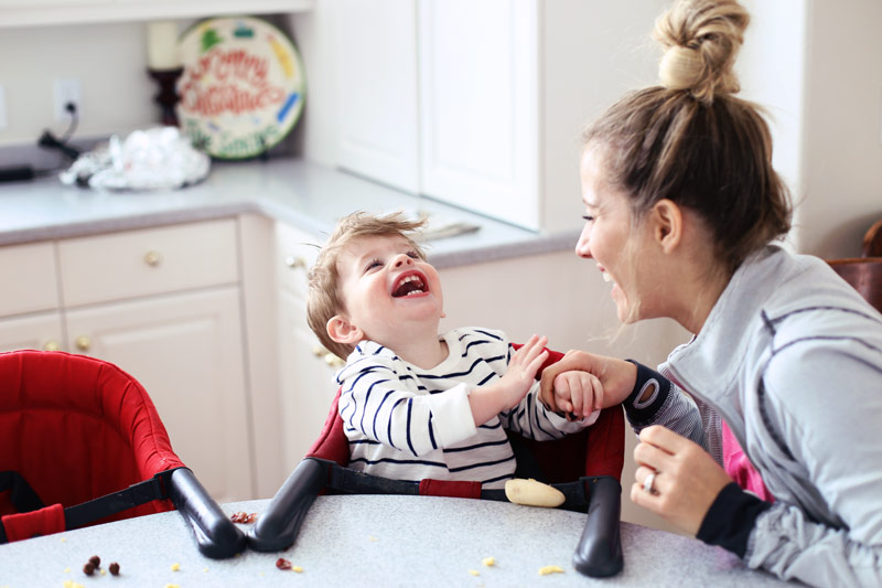 Laughing with her 18-month-old son, Abby sits at a table.